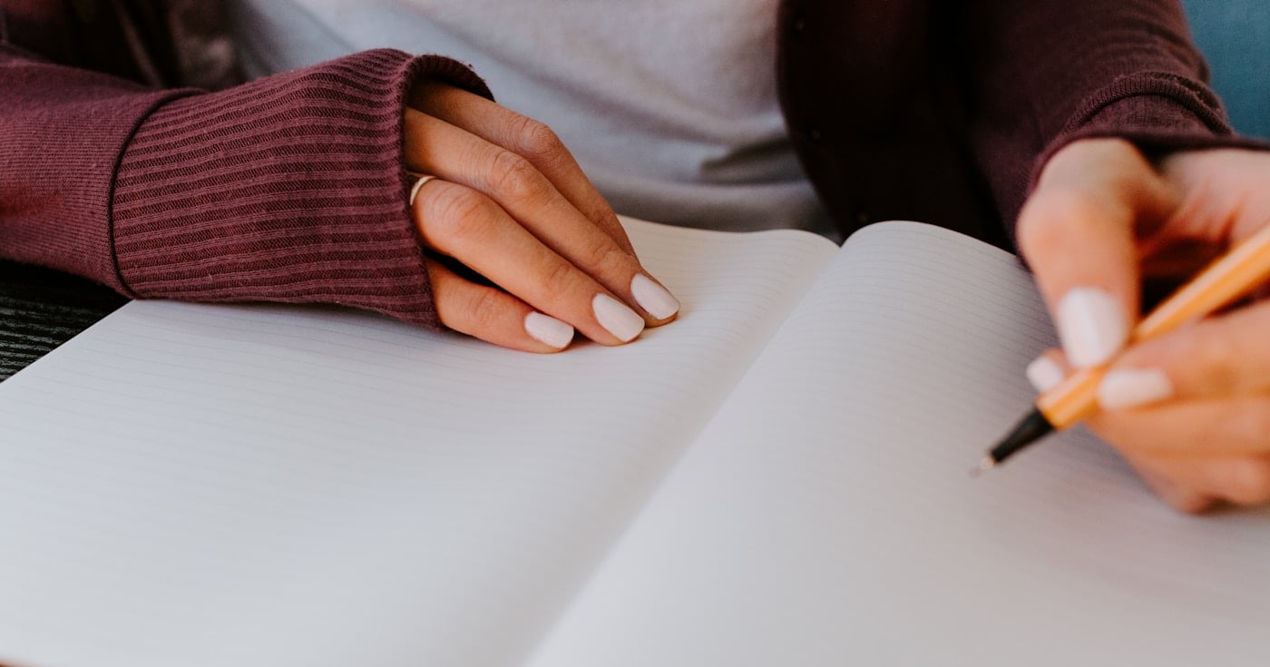 Person writing in a blank notebook at a desk