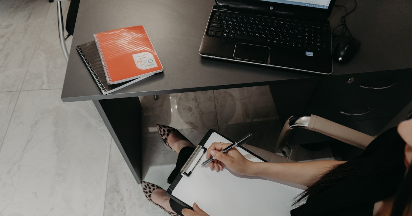 Person writing a proposal cover letter at a desk with a laptop