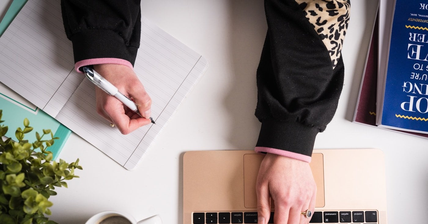 Writer working in journal on desk with coffee and book